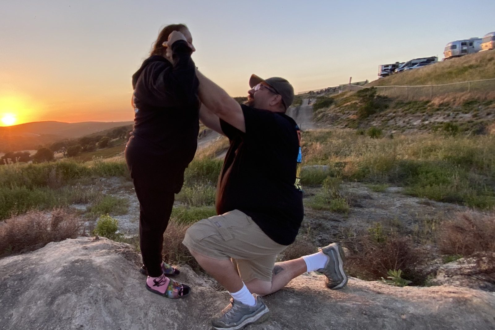 Sean on one knee proposing to Jen on a hilltop at sunset